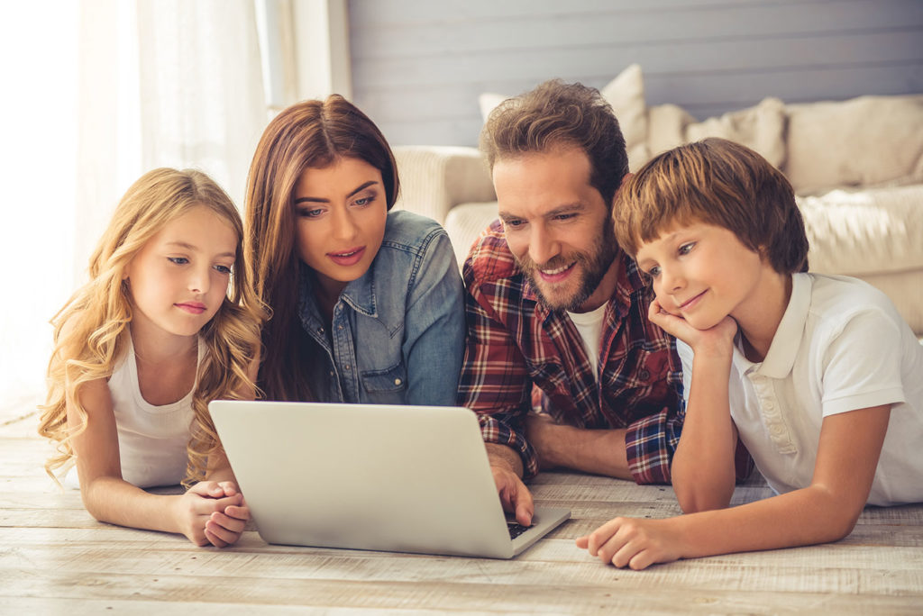 family of four laying on the floor looking at a laptop
