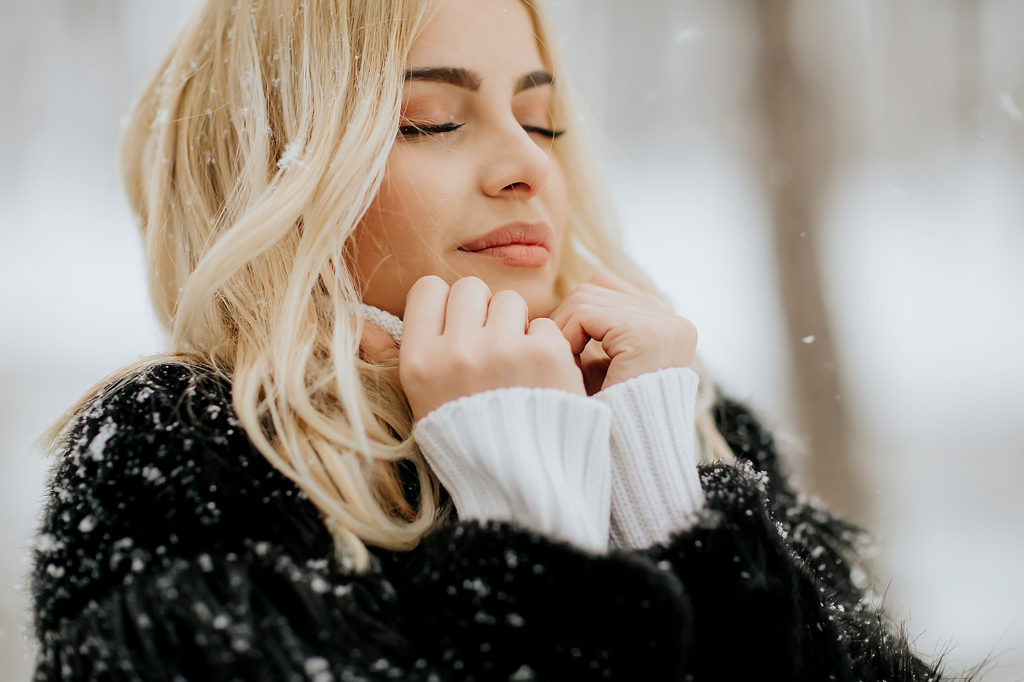 winter beauty survival guide: blonde woman standing in woods with snow