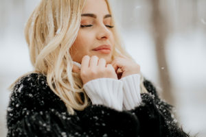 winter beauty survival guide: blonde woman standing in woods with snow