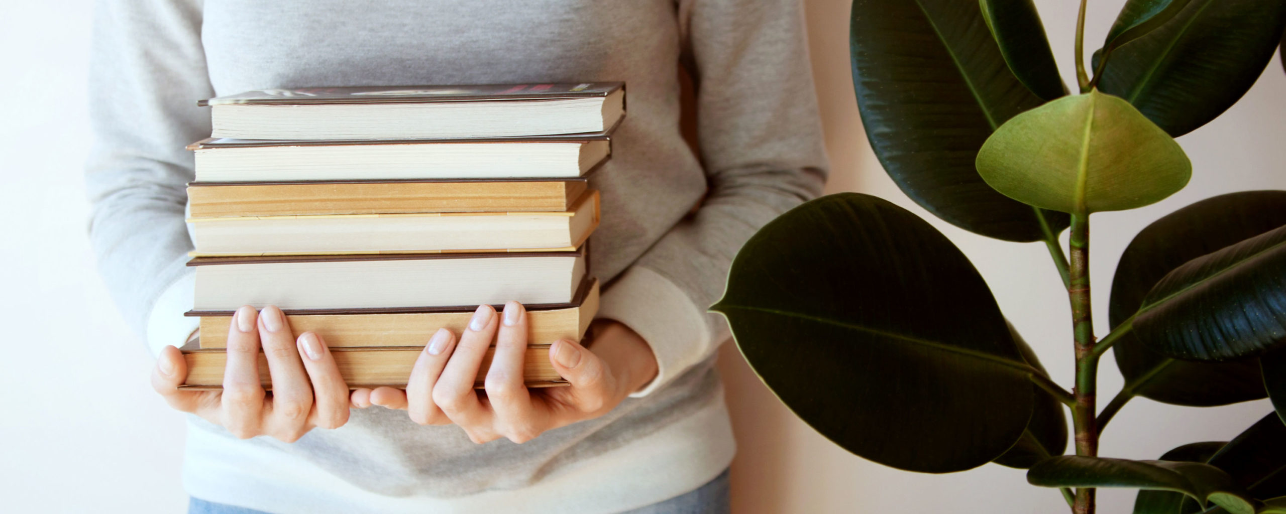 photo: girl holding stack of books standing beside large green plant