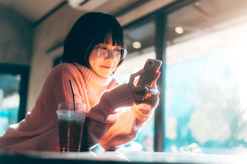 Young adult happy asian woman wear eyeglasses using mobile phone for social media application